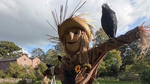 A happy scarecrow with a red brick building in the background